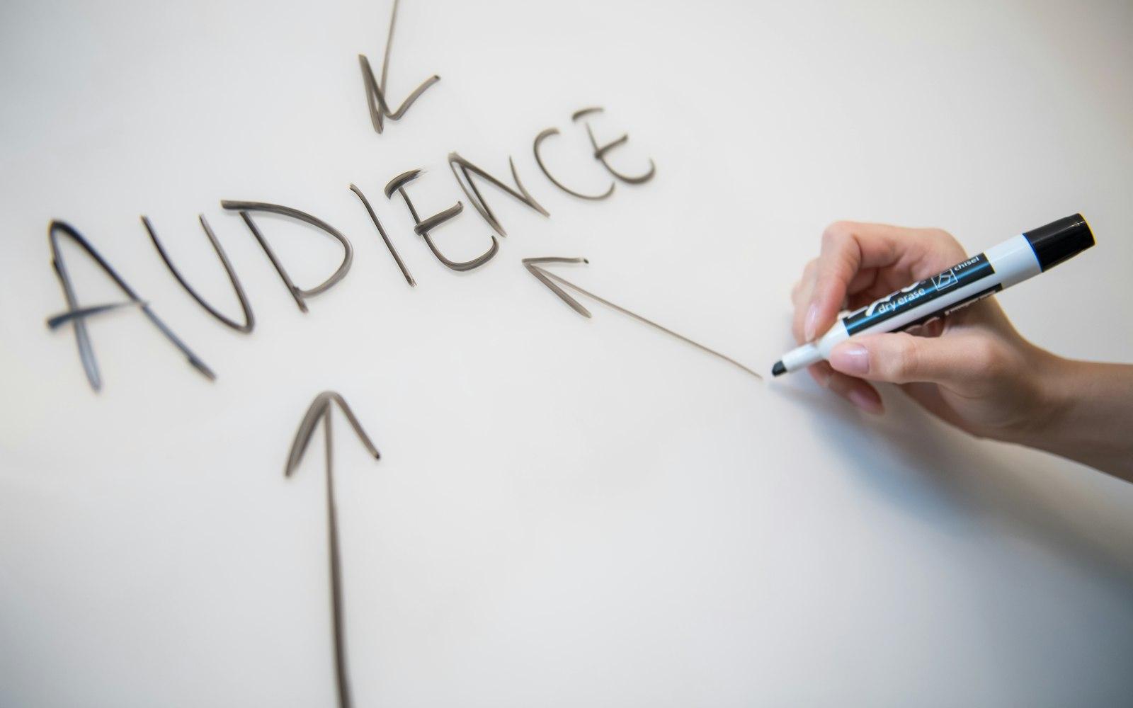 A hand writing the word audience on a whiteboard