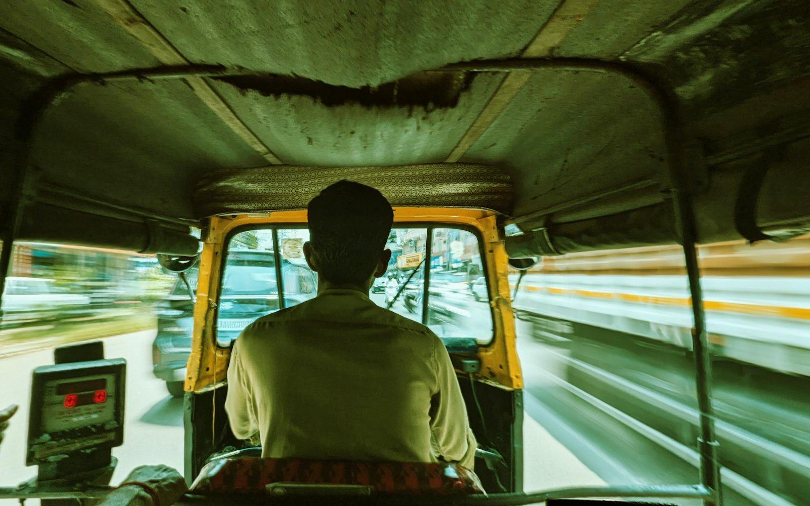 An auto rickshaw driver moving through a blurred street